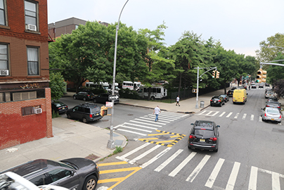 A photograph of a New York City intersection treated with left turn traffic calming in the form of a slow turn wedge.